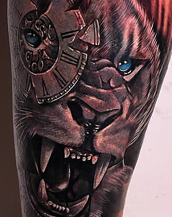 Después del cover-up: león rugiendo con un reloj roto y ojo azul, en realismo, que tapa por completo el tatuaje anterior