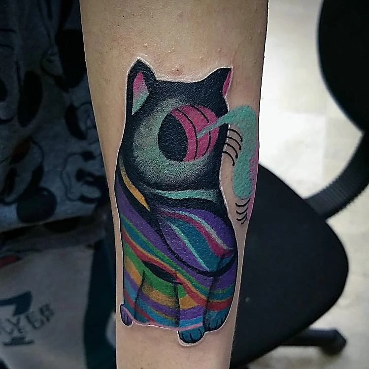 Gato surrealista con franjas multicolor y una esfera rosa en el ojo, en el antebrazo