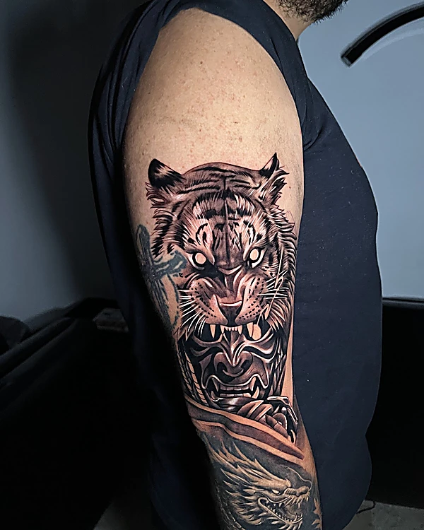 Tigre rugiendo sobre una máscara hannya en negro y gris, en el brazo, con un dragón en el codo